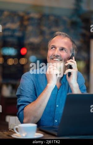 Homme d'affaires attentionné avec la main sur le menton parlant sur le téléphone mobile dans le café Banque D'Images