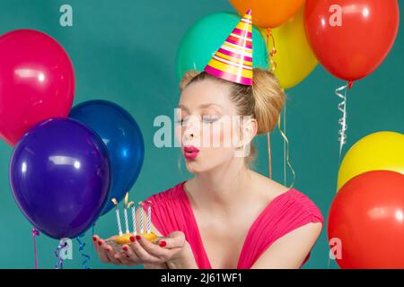 Jeune femme portant un chapeau de fête soufflant des bougies sur le gâteau d'anniversaire sur fond vert Banque D'Images