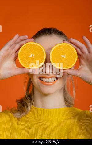 Jeune femme souriante couvrant les yeux avec une tranche d'oranges Banque D'Images