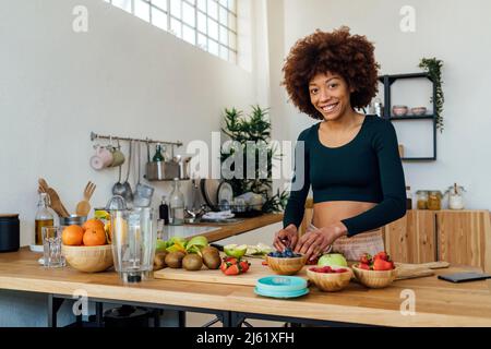 Bonne jeune femme avec des fruits frais à la table dans la cuisine Banque D'Images