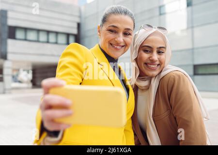 Une femme d'affaires heureuse qui prend son selfie avec un jeune collègue par le biais d'un téléphone intelligent Banque D'Images