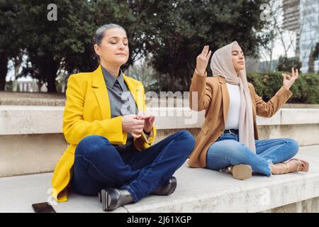 Femmes d'affaires pratiquant l'exercice de respiration assis sur les pattes croisées sur les marches Banque D'Images