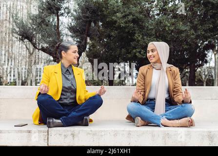 Des femmes d'affaires souriantes assises sur les jambes, regardant les unes les autres sur les marches Banque D'Images