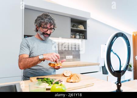Un homme de premier plan souriant fait un sandwich avec croissant et se vante sur un smartphone à la maison Banque D'Images