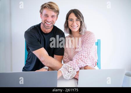 Homme et femme heureux assis avec des ordinateurs portables à la table Banque D'Images