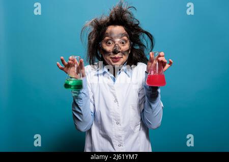 Un chimiste fou tenant des flacons en verre remplis de composés chimiques toxiques après une explosion en laboratoire. Travailleur de laboratoire fou et fou ayant rempli des béchers de substances liquides après un échec d'expérience en laboratoire Banque D'Images