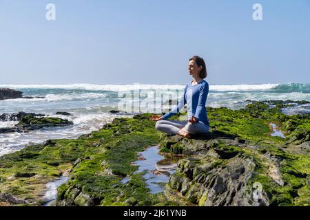 Femme assise en position lotus et méditant sur le rocher à la plage Banque D'Images