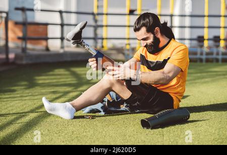 Athlète souriant portant une jambe prothétique assise sur l'herbe Banque D'Images