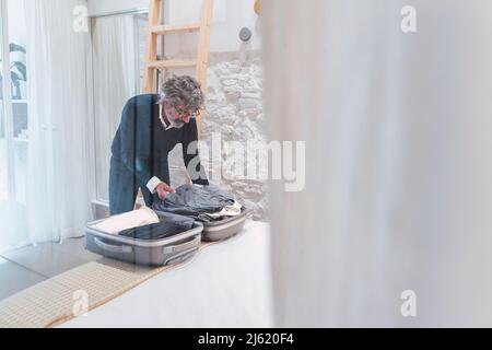 Valise d'emballage indépendante senior dans la chambre vue à travers le verre Banque D'Images