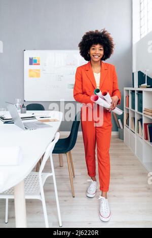 Femme d'affaires souriante tenant un plan d'action au bureau Banque D'Images