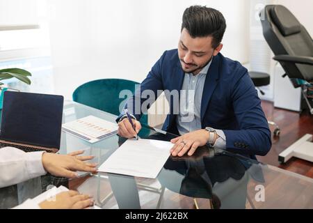 Homme signant sur papier assis avec un médecin à la clinique Banque D'Images