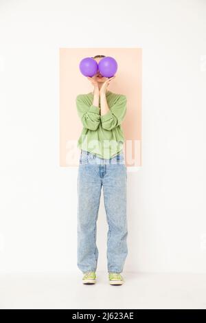 Jeune femme couvrant le visage avec des ballons violets debout sur fond blanc Banque D'Images