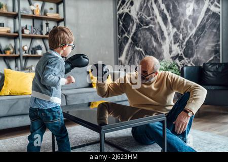 Grand-père et petit-fils joueurs portant des gants de boxe jouant dans la salle de séjour à la maison Banque D'Images