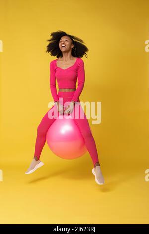 Jeune femme joueur avec le ballon rose sautant sur fond jaune Banque D'Images