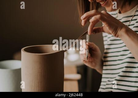 Artisan coupant l'excès d'argile du pot avec un outil à main à l'atelier Banque D'Images