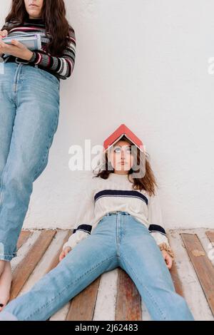 Femme ennuyée avec livre sur la tête inclinable devant le mur blanc à l'arrière cour Banque D'Images