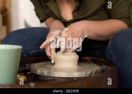 Mains de la femme faisant pot avec de l'argile sur la roue de poterie à l'atelier Banque D'Images