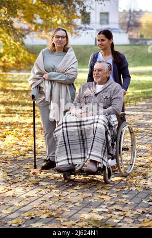 Femme âgée parlant avec une infirmière et un homme handicapé assis en fauteuil roulant au parc Banque D'Images