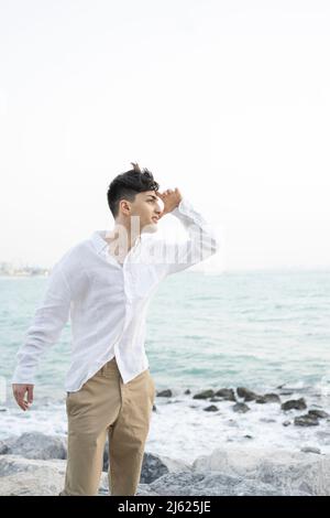 Jeune homme regardant la distance debout sur la plage rocheuse Banque D'Images