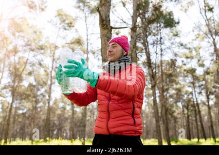 Homme portant un chapeau en tricot tenant des bouteilles en plastique dans la forêt Banque D'Images