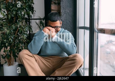 Jeune homme heureux portant des lunettes de vue assis près de la fenêtre à la maison Banque D'Images