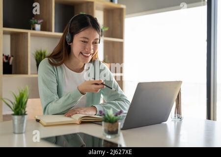 Concentrez-vous asiatique gial freelance portant un casque, communiquant avec le client via un appel vidéo sur ordinateur. Tuteur féminin professionnel agréable millénaire Banque D'Images