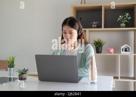 Concentrez-vous asiatique gial freelance portant un casque, communiquant avec le client via un appel vidéo sur ordinateur. Tuteur féminin professionnel agréable millénaire Banque D'Images