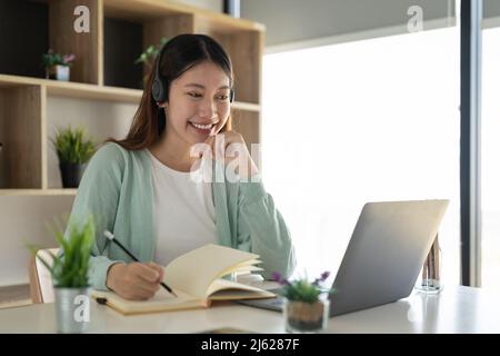 Concentrez-vous asiatique gial freelance portant un casque, communiquant avec le client via un appel vidéo sur ordinateur. Tuteur féminin professionnel agréable millénaire Banque D'Images