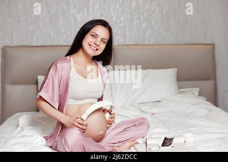 Pregnant woman holding casque sur son ventre Banque D'Images