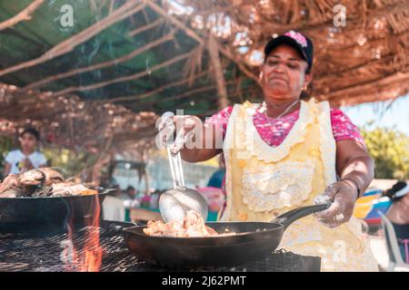 Photo verticale d'une femme latine âgée qui prépare du poisson frit sur la plage de Masachapa, au Nicaragua. Concept des métiers, du travail et de l'activité des personnes âgées Banque D'Images