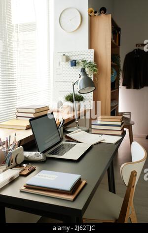 Lieu de travail moderne de l'étudiant composé de lampe électrique, livres, carnet, ordinateur portable et fournitures de bureau contre fenêtre avec stores Banque D'Images