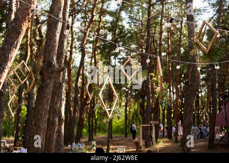 Réception de mariage à l'extérieur dans la forêt de pins. Tables à manger, bancs décorés dans le style boho avec bougies, fleurs, lumières de fée printanière, assiettes Banque D'Images