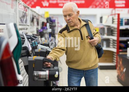 Homme âgé à la recherche d'un aspirateur vertical au comptoir dans la salle d'exposition du service d'hypermarché des appareils électriques Banque D'Images