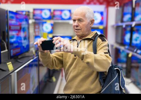 Senor homme pensionné scannant code QR télévision numérique moderne avec Smart tv dans la salle d'exposition du magasin de produits électroniques numériques Banque D'Images