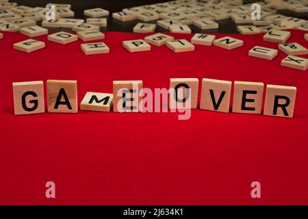 Phrase « Game Over » composée de plaques de bois avec des lettres sur fond de feutre rouge Banque D'Images