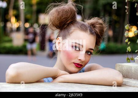 Une jeune fille avec un maquillage clair épingler se tient dans le parc penchée sur une clôture Banque D'Images