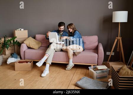 Un jeune homme et une femme se détendent ensemble sur un canapé en train de manger une pizza dans le salon loft après avoir changé de maison Banque D'Images