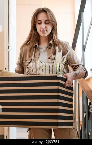 Plan vertical moyen d'une jeune femme se déplaçant dans une autre maison allant en bas porte-boîte avec la maison en elle Banque D'Images