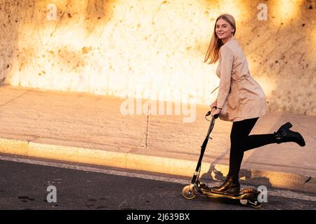 Jeune femme en train de rouler en scooter électrique. Nouveau transport urbain moderne et écologique. Écologie et concept de travail. Banque D'Images