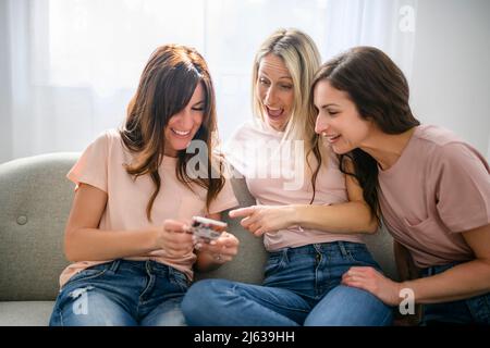 Trois joyeuse femme utilisant un smartphone mobile à la maison assis sur un canapé Banque D'Images