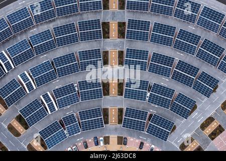 Vue aérienne directement au-dessus des rangées de panneaux solaires sur le toit d'un parc et de conduire un parking générant de l'énergie renouvelable propre dans un environnement de ville Banque D'Images