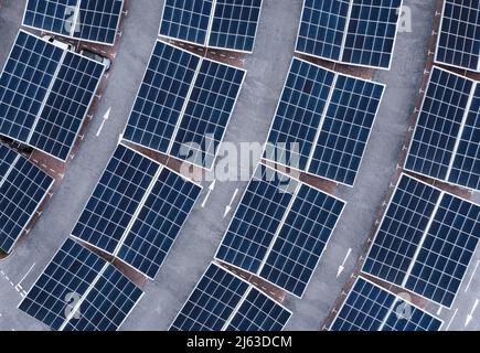 Vue aérienne directement au-dessus des rangées de panneaux solaires sur les toits d'un parking de voitures générant de l'électricité propre renouvelable dans une ville Banque D'Images