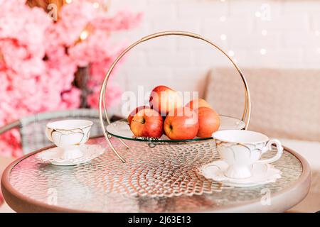 Un vase de pommes et deux tasses de thé sur une table en verre Banque D'Images