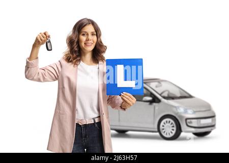 Jeune femme tenant des clés de voiture et une plaque d'étudiant devant une voiture argentée isolée sur fond blanc Banque D'Images