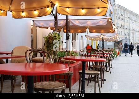 Café de rue avec tables rouges et chaises en bois vintage en plein air, décoré avec des lumières festives Banque D'Images