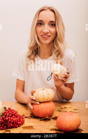 Une jeune femme tient des citrouilles dans ses mains et s'assoit à la table dans la cuisine Banque D'Images