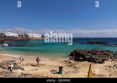 Scène de plage avec des personnes qui nagent et bronzer autour de Costa Teguise, Lanzarote. Mer calme, bleu-vert clair et ciel bleu. Banque D'Images