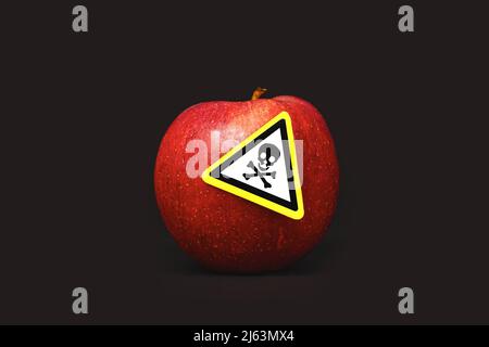 Concept des résidus de pesticides dans les produits alimentaires agricoles dangereux pour l'homme. Une pomme rouge avec un autocollant symbole de poison sur fond noir Banque D'Images