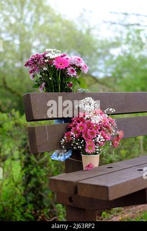 Fleurs laissées sur un banc à la mémoire d'un être cher. Banque D'Images