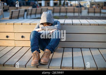 Un adolescent solitaire et triste dans un capot, dans une pose fermée se cachant des problèmes dans la rue dans un environnement urbain. Banque D'Images